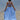 girl in a light blue dress standing on a beach with boats in the background