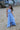 Young girl in a blue dress standing on a sandy beach.